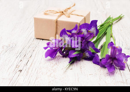 Blumenstrauß aus lila Blumen Iris und Geschenk auf einem hellen Hintergrund. Geringe Tiefenschärfe Stockfoto