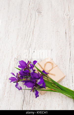 Blumenstrauß aus lila Blumen Iris und Geschenk auf einem hellen Hintergrund. vertikale Foto. Geringe Tiefenschärfe Stockfoto