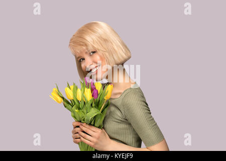 Schöne begeistert lächelnde Frau mit einem Blumenstrauß aus Tulpen auf grauem Hintergrund Stockfoto