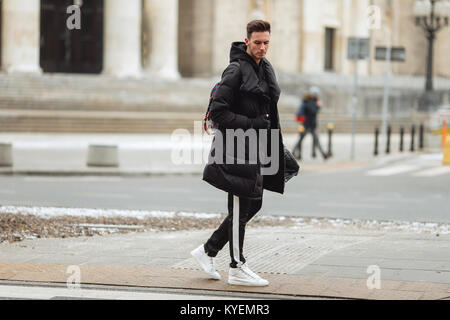 Stilvolle Mann wolk auf der Straße. Winter kalt Outfit. Große Jacke mit weißen Turnschuhen. Blured Hintergrund Straße. Profecional Modell Foto. Stockfoto