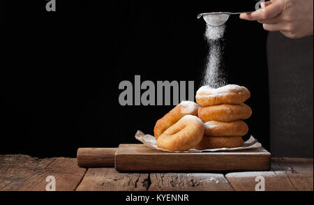 Baker Streuseln süße Krapfen mit Puderzucker auf schwarzem Hintergrund. Lecker, aber ungesunden Essen auf dem alten Holztisch mit kopieren. Stockfoto