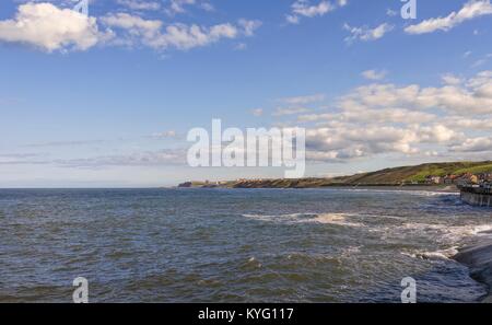 Der Blick Richtung Whitby aus sandsend. Während die Wellen gegen die Ufermauer im Sandsend, Whitby Harbour kann am Horizont gesehen werden. Stockfoto