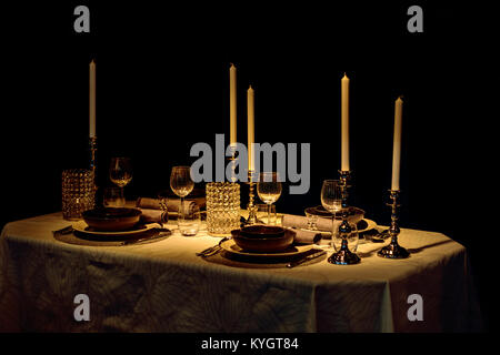Gedeckter Tisch mit Weingläsern und Kerzen auf einem dunklen Hintergrund, durch helle Lampe Licht beleuchtet. Stockfoto