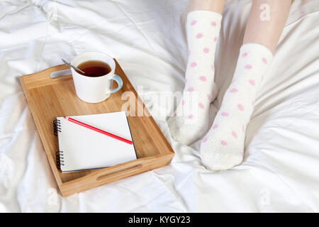 Ein Tablett mit einer Tasse Kaffee, einem Notizblock und Bleistift steht auf dem Bett Stockfoto