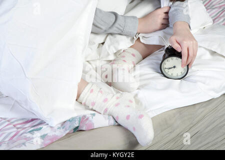 Die Mädchen, die in einer weißen Decke gewickelt, legt ihr die Hand, um den Alarm auszuschalten. Es gibt acht Stunden auf den Wecker. Stockfoto