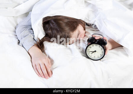 Die Mädchen, die in einer weißen Decke gewickelt, legt ihr die Hand, um den Alarm auszuschalten. Es gibt acht Stunden auf den Wecker. Stockfoto