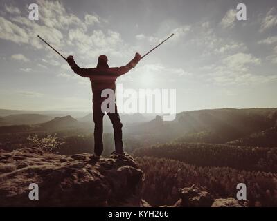 Wanderer mit Medizin Krücke über den Kopf erreicht persönliches Ziel. Gebrochenes Bein" in "Wegfahrsperre Tief nebligen Tal unten Silhouette der Mann mit der Hand fest Stockfoto