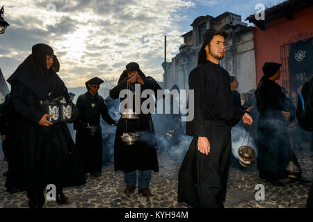 Antigua, Guatemala - 19. April 2014: Mann in schwarzen Roben und Hauben Räucherwerk verbreiten sich in einer Strasse der Stadt Antigua während einer Prozession der Stockfoto