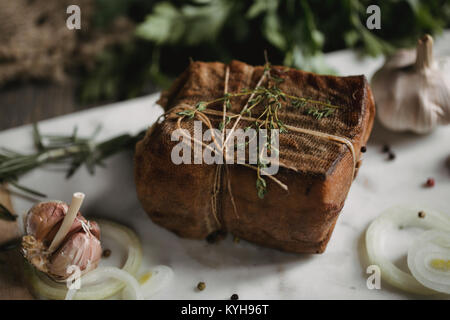 Klumpen von gesalzenem geräucherten Speck in Gaze mit einem Seil. Traditionelle russische und ukrainische Mahlzeit. Gesundes Essen mit pranami Gewürze, Kräuter, Zwiebel und Knoblauch. Stockfoto