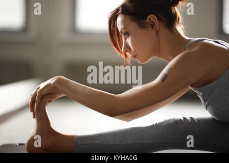 Junge sportliche Frau Yoga Stretching Übung sitzen in der Turnhalle in der Nähe von hellen Fenstern. Stockfoto