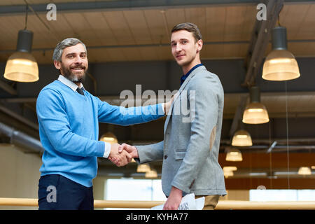 Taille bis Portrait von zwei erfolgreichen Geschäftspartner schütteln Hände an der Kamera auf der Suche nach dem Schließen wichtige Geschäft gegen den Hintergrund der offi Stockfoto