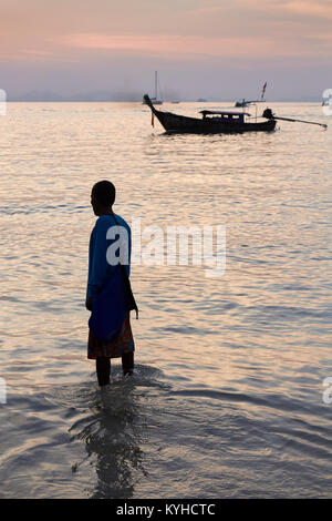 Ein Mann mit einem Longtailboot bei Sonnenuntergang, West Railay Beach, Krabi, Thailand Stockfoto