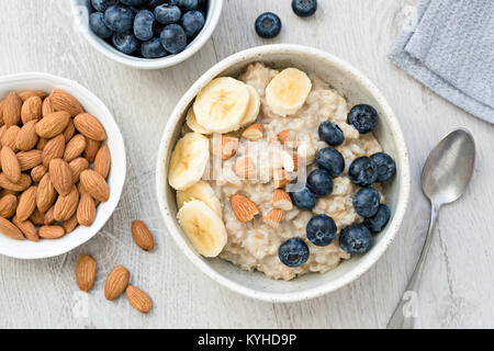 Haferflocken Porridge mit Bananen, Mandeln und Blaubeeren in weiße Schüssel. Tabelle Ansicht von oben. Gesundes Essen, gesundes Essen und Diäten Konzept Stockfoto