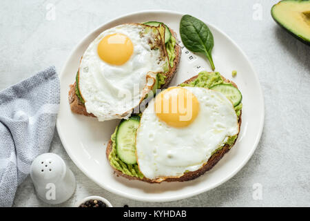 Frühstück Toast mit Spiegelei, Avocado und Gurke mit Vollkornbrot auf weiße Platte. Gesundes Frühstück essen Stockfoto