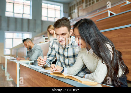 Porträt von zwei fröhliche Studenten am Schreibtisch sitzen im Hörsaal der modernen Hochschule, junger Mann und die asiatische Frau mit Klasse, kopieren Raum Stockfoto