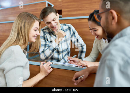 Internationalen Gruppe von Studenten um Schreibtisch in modernen Hörsaal sitzen und miteinander studiert, glücklich lächelnd und Notizen zu machen Stockfoto