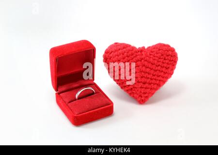 Rote gehäkelte Herz mit Ehering in einem Kasten auf dem isolierten weißen Hintergrund. Valentinstag. Symbol der Liebe. Stockfoto