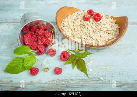 Frische Himbeeren in einen Eimer und Haferflocken in eine hölzerne Schüssel auf eine rustikale Holz- Hintergrund. Gesunde Ernährung, Vegetarische Konzept Stockfoto