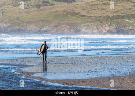 Polzeath surfen - ein Surfer zu Fuß aus dem Meer auf Polzeath Strand an der Küste von North Cornwall. Stockfoto