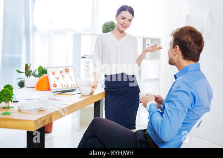 Schöne junge Frau, die vor ihrer Kollegin, während im Gespräch Stockfoto