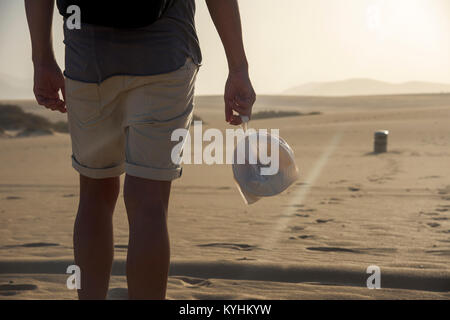 Nahaufnahme eines jungen Backpacker Mann in kurzen Hosen hinter einer durchsichtigen Plastikbeutel mit Resten, während er durch den Sand gesehen Stockfoto