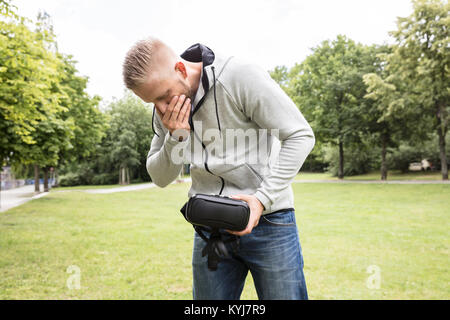 Junger Mann mit Übelkeit Holding Virtual Reality Headset im Park Stockfoto