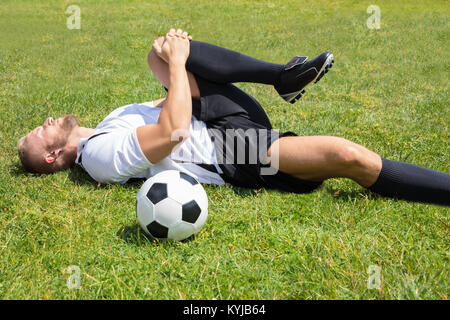 Nahaufnahme der männlichen Fußball-Spieler Leiden Knieverletzung liegen auf Feld Stockfoto