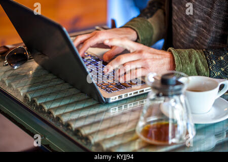 Die Hände des kaukasischen Mann Typ auf Laptop mit Kaffeebecher und Kaffeetasse neben ihm in einem Café mit Fokus auf der Tastatur Stockfoto