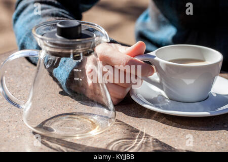 Kaukasische Frau Hand hält Keramik Tasse mit schwarzem Tee und Milch, leeres Glas Teekanne neben Stockfoto