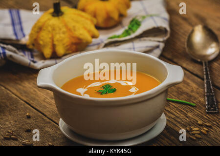 Kürbis und Karotten Suppe mit Sahne in Weiß Schüssel auf Holz Tisch Stockfoto