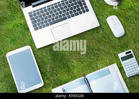 Erhöhten Blick auf elektronische Geräte mit Tagebuch auf grünem Gras Stockfoto