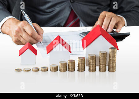 Unternehmer Berechnung der Steuer Vor dem Haus Modelle und gestapelte Münzen Stockfoto
