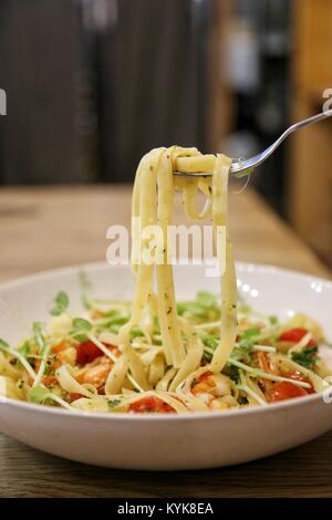 Mit Edelstahl Gabel pick Pasta/knausern Linguine mit Scampi in einem weißen Teller auf einen hölzernen Tisch oben Stockfoto