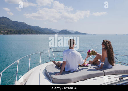 Paar beim Flitterwochen an Bord der luxuriösen Yacht, luxuriöse Yacht in tropischen Meer, Mann und Frau trinkt Kokosnüsse und Entspannen Stockfoto