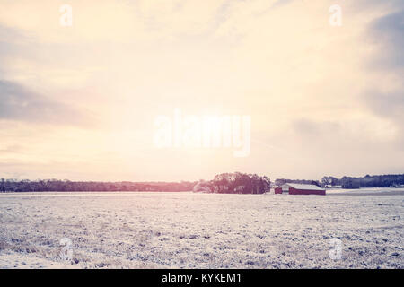 Ländliche Landschaft mit einem roten Scheune auf einem Feld mit Schnee in den Sonnenaufgang abgedeckt Stockfoto