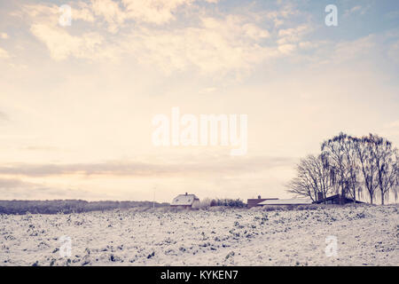 Die winterliche Landschaft mit einem kleinen Bauernhof auf einem ländlichen Gebiet mit Schnee im Sunrise Stockfoto