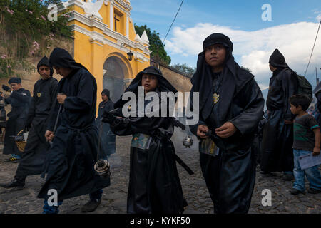 Antigua, Guatemala - 19. April 2014: Junge Männer in schwarzen Roben und Hauben Räucherwerk verbreiten sich in einer Strasse der Stadt Antigua während einer Prozession Stockfoto