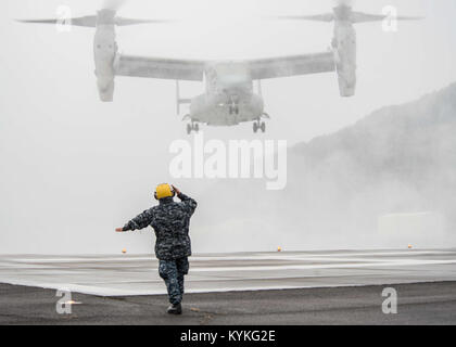 SASEBO, Japan (31. 16, 2017) der Bootsmann Mate 1. Klasse Carlglo Rula leitet eine MV-22 Osprey zu Marine Medium Tiltrotor Squadron 262 (VMM-262), Commander, US-Flotte Aktivitäten Sasebo zugeordnet. Die Osprey transportiert Leiter der Marineoperationen Adm. John Richardson zum und vom KFBS für seinen Besuch der Installation. (U.S. Marine Foto von Mass Communication Specialist 3. Klasse Geoffrey S. Barham/Freigegeben) 171216-N-SD 711-0023 Stockfoto