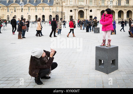 PARIS - Jan. 5, 2014: Eine nicht identifizierte Kind stellt für ein Bild, während auf einem Podest im Innenhof des Louvre Museum stehen. Ihre Mutter cr Stockfoto