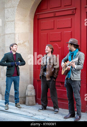 PARIS - Jan 2 2014: unbekannter Straßenmusiker spielt vor einer roten Tür in dem historischen Viertel Le Marais. Stockfoto