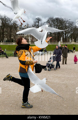 PARIS - Jan 4, 2014: Eine nicht identifizierte Frau wirft Essen in die Luft für die Vögel an den Luxembourg Gärten, eine beliebte Aktivität für Besucher am Stockfoto