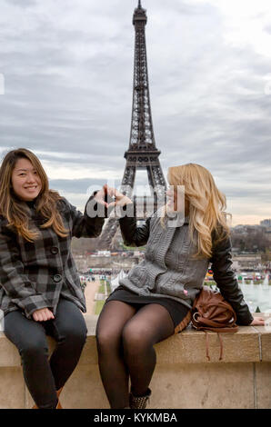 Paris Eiffel Tower Touristen posieren für Fotos mit dem Turm im Hintergrund. Zwei lächelnde junge Frauen bilden eine Herzform mit ihren Händen. Stockfoto