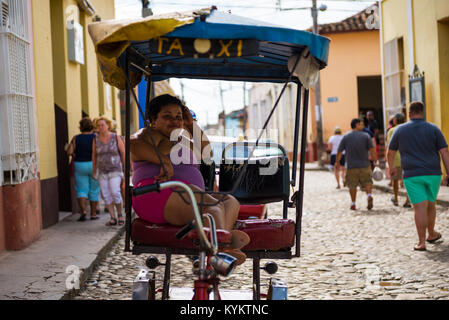 Trinidad, Kuba - 26. November 2015: Ein lächelndes kubanische Frau sitzt in einem Pedal Bike Taxi, während die Leute gehen in den Straßen hinter ihr Stockfoto