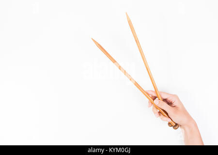 Frau hand mit zwei hölzernen Stricknadeln auf weißen Hintergrund. Stockfoto