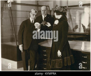 Historische Illustration mit Männern und einer Frau in zeitgemäßer Mode, die vor einem Gehäuse stehen, das Teil des National Museum of the American Indian Collection ist. Stockfoto