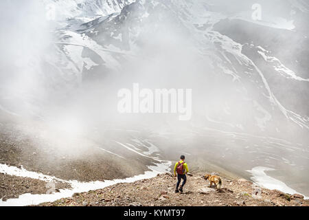 Wanderer in grünes T-Shirt mit Rucksack und hundewiesen in der schneebedeckten Berge an nebligen Himmel Hintergrund Stockfoto