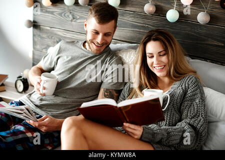 Glückliches junges Paar mit Kaffee Lesen im Bett Stockfoto