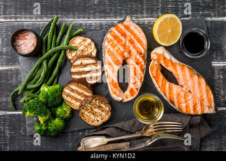 Schiefer Platte mit gegrilltem Lachs Steaks und Gemüse auf schwarzen Holztisch, Ansicht von oben Stockfoto