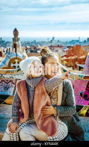 Barcelona-Handschrift. Porträt des Lächelns moderne Mutter und Tochter Touristen in Barcelona, Spanien zeigt auf etwas sitzen auf einer Bank Stockfoto