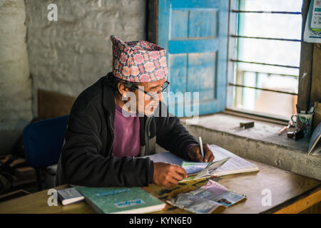 Die Sekretärin schreibt Informationen über den Touristen zu einem Buch im Büro im Dorf Dhampus, Nepal, Asien. Annapurna Base Camp Trek. Stockfoto